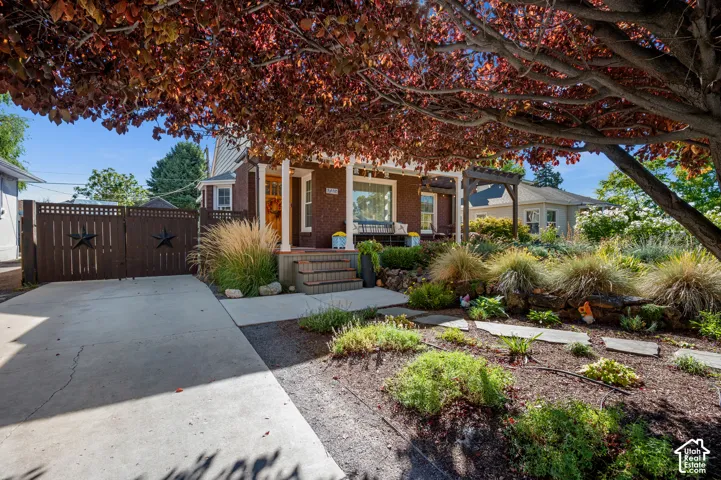 Brick exterior with a covered porch, established landscaping, and a driveway with a privacy gate