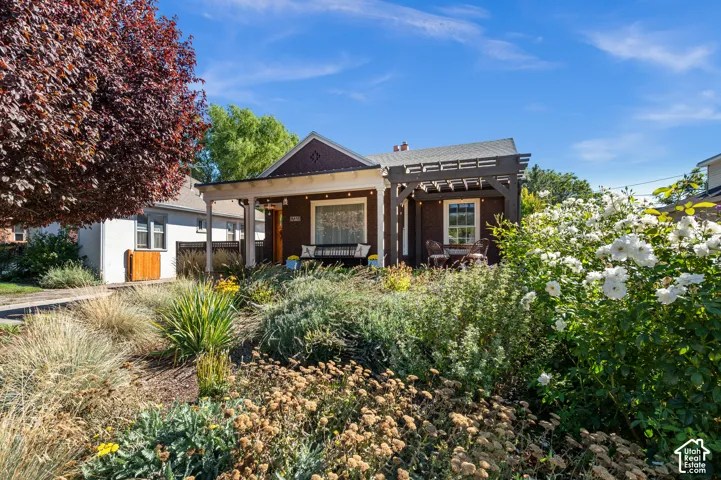 Stone facade residence featuring a covered front porch, a side pergola, and mature landscaping