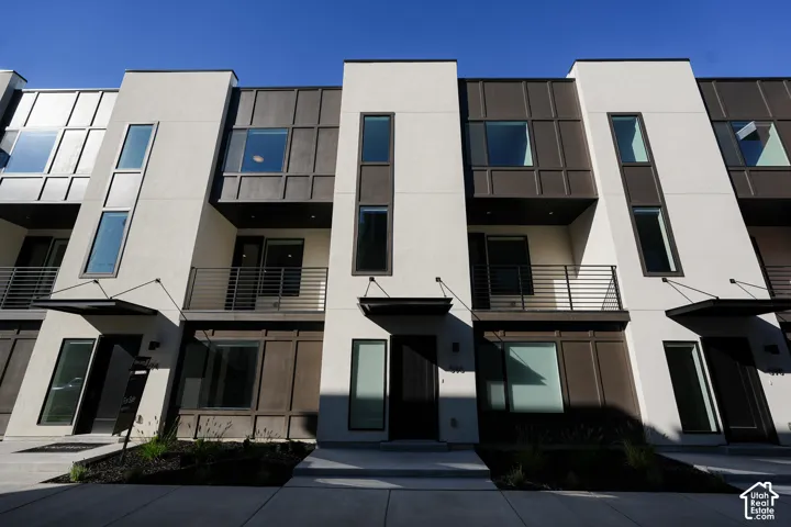 Contemporary exterior featuring smooth stucco finish, vertical panel siding, dark metal awnings, and integrated balconies with horizontal railings