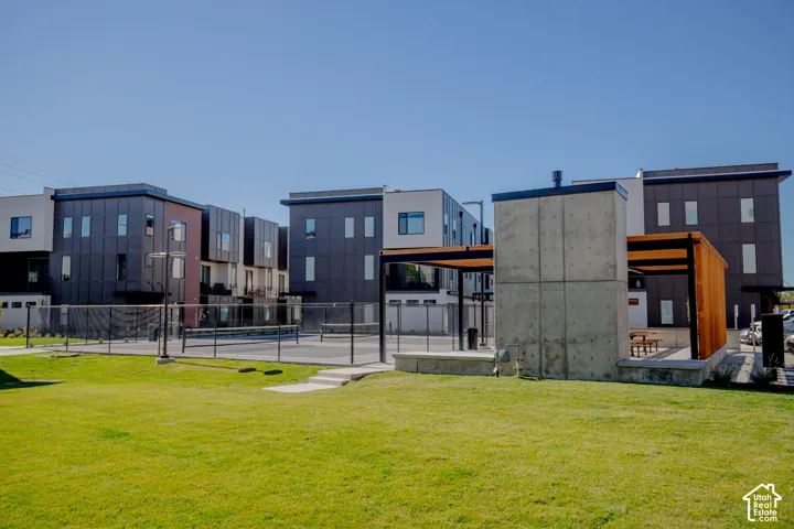 Common recreation area featuring a paved sports court, concrete masonry structure with wood-frame trellis, and expansive lawn