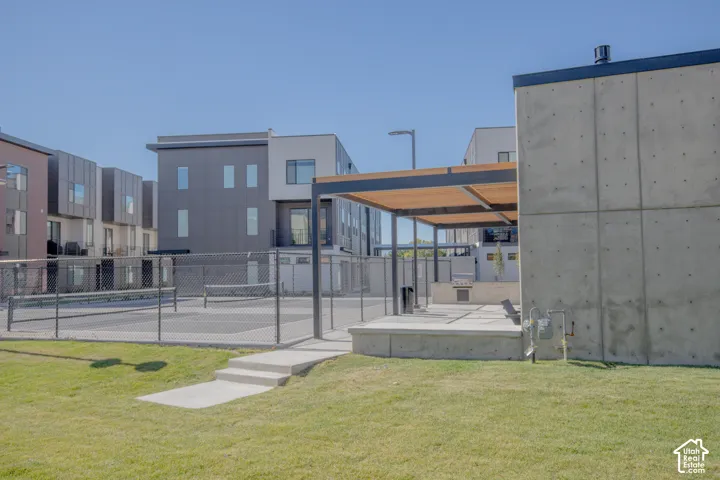 Fenced sport court featuring a concrete pavilion with built-in grill and covered patio area, situated on a manicured lawn