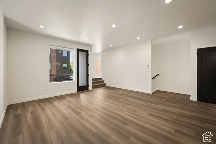Spacious room with wood-finish flooring, recessed lighting, a large window, a glass-paneled door, and a solid black door