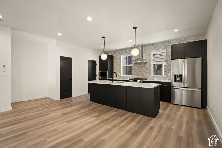 Modern kitchen featuring an island with white countertops, stainless steel appliances, dark cabinetry, and a full-height tile backsplash