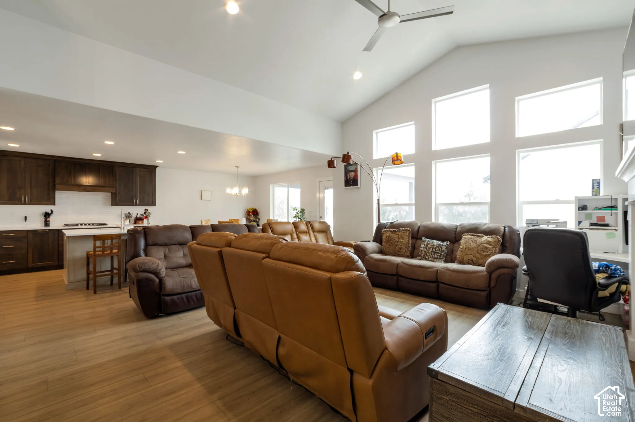 Vaulted ceiling with a ceiling fan, light wood-finish flooring, recessed lighting, white walls, and a kitchen featuring dark wood cabinetry, white countertops, and a white subway tile backsplash