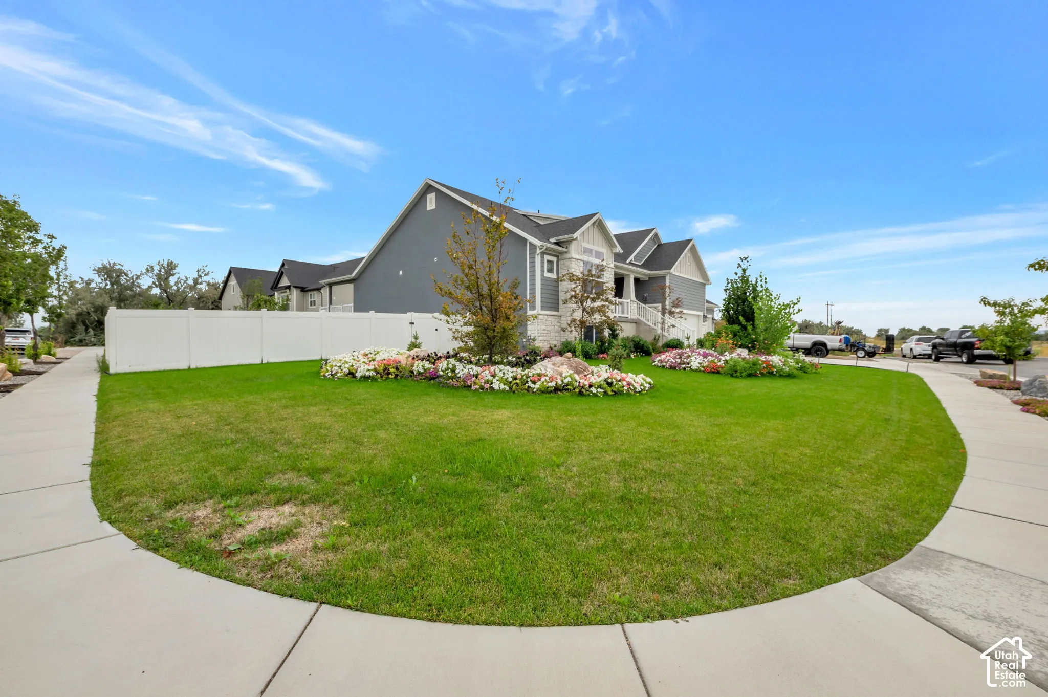 Manicured lawn with mature landscaping, concrete sidewalks, and a white privacy fence