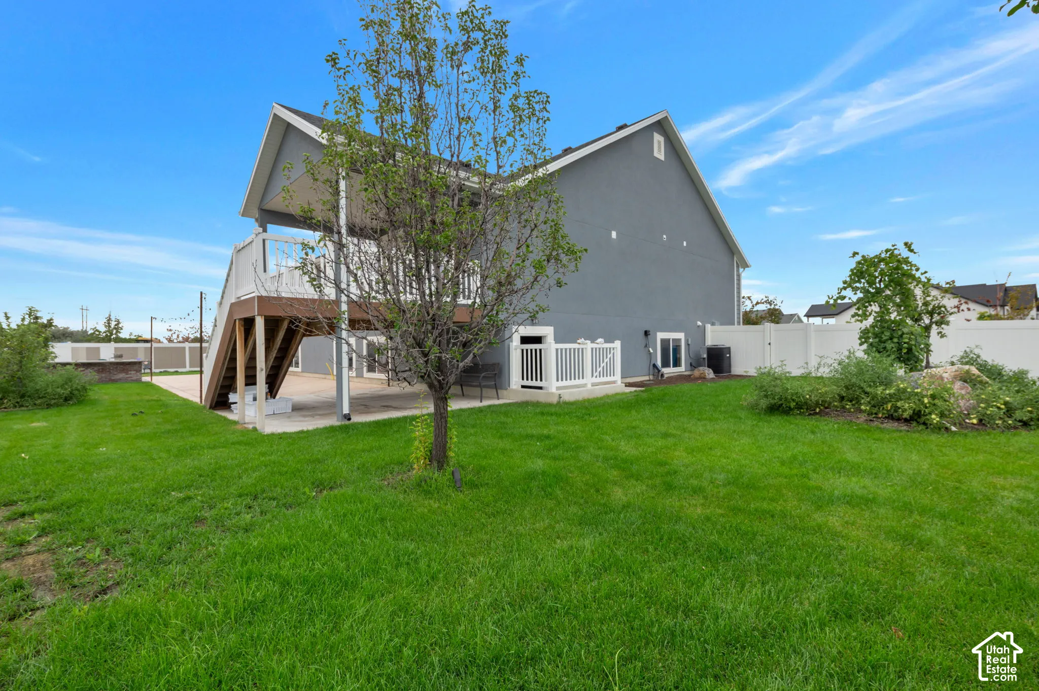 Expansive green lawn with a two-story exterior featuring a covered deck and a ground-level patio