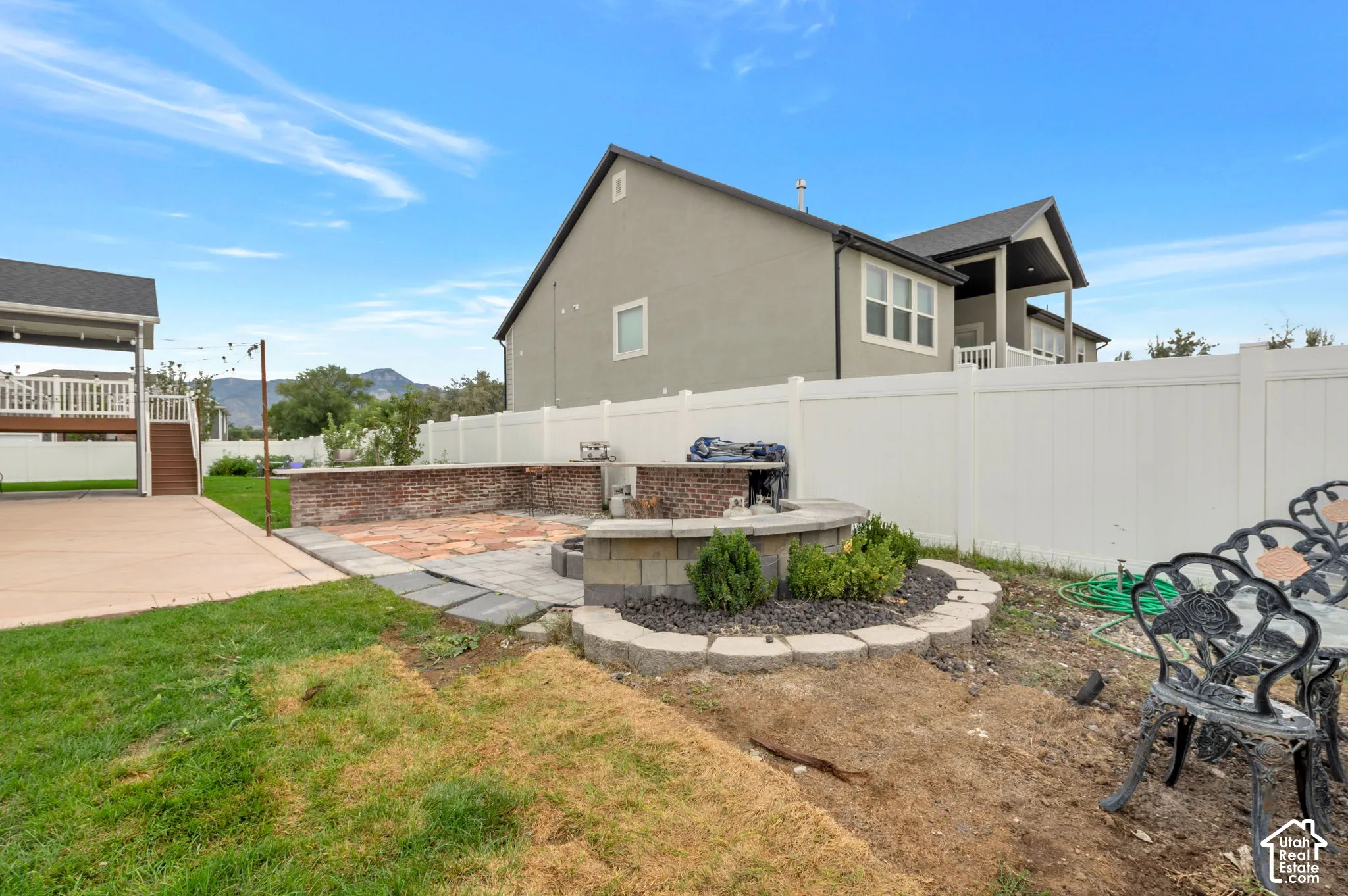Spacious backyard featuring a built-in fire pit, paved patio, and a covered deck with white railing
