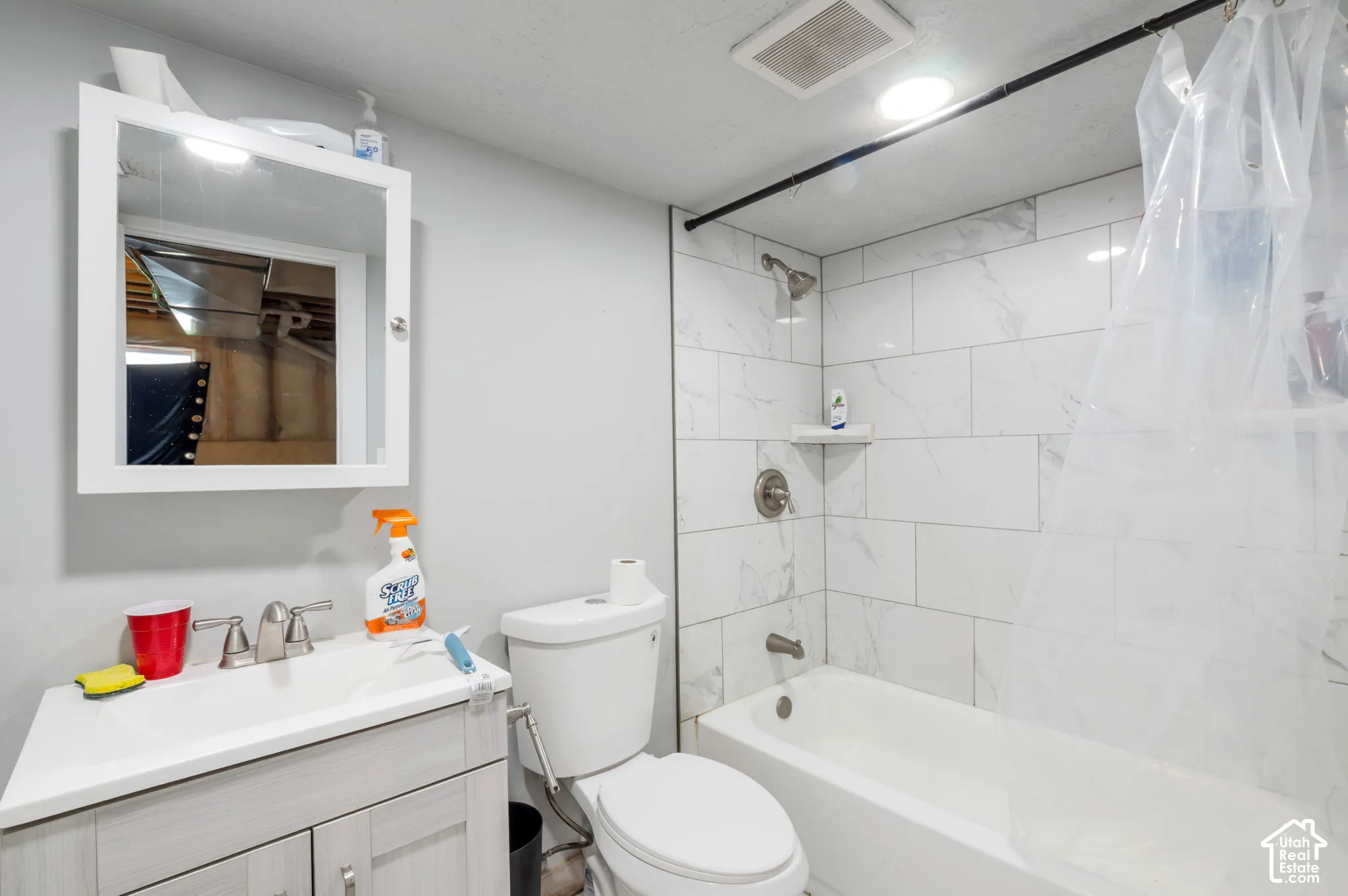 Bathroom featuring a white vanity with integrated sink, wall-mounted medicine cabinet, white toilet, and a bathtub with white subway tile surround