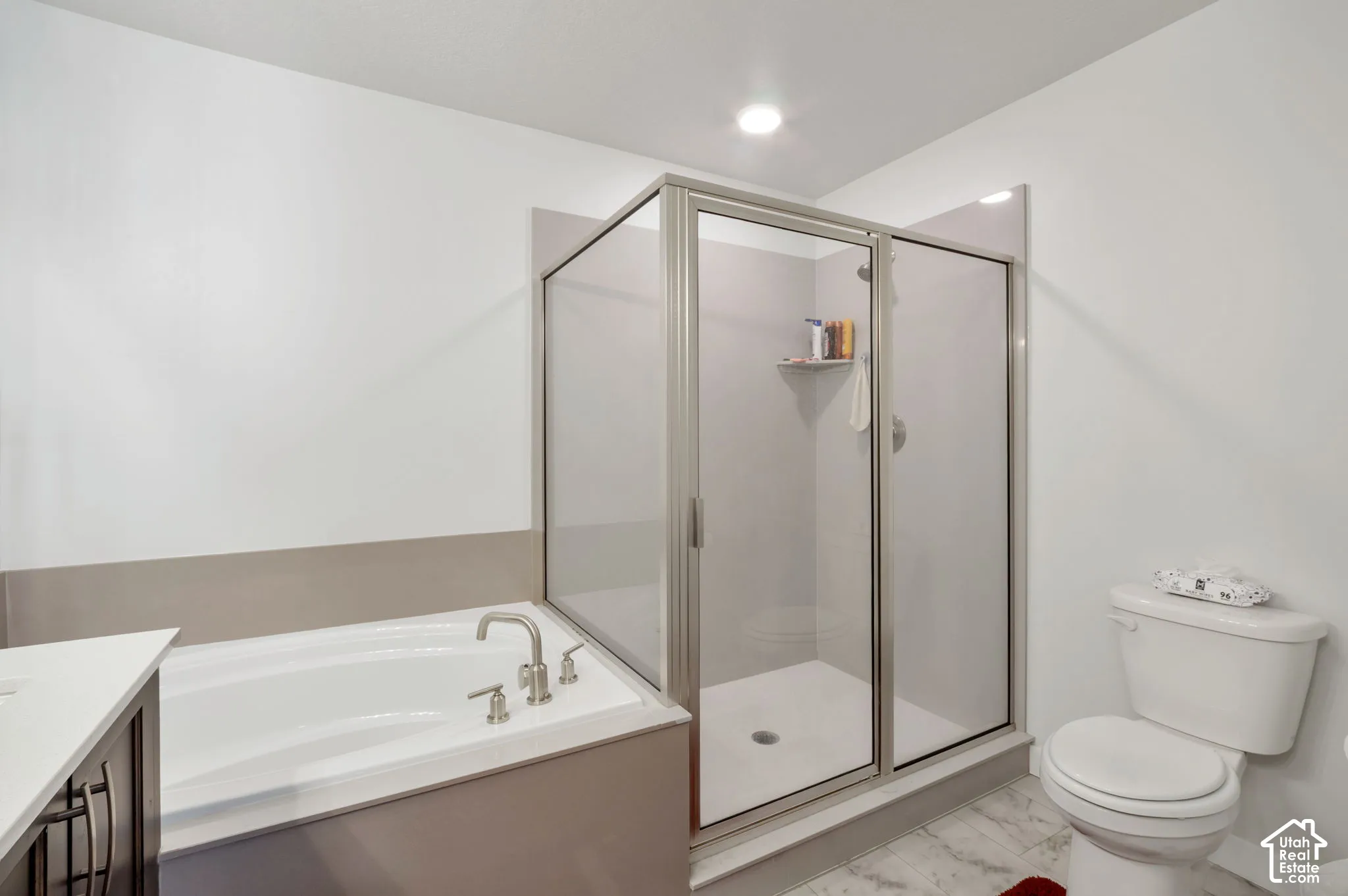 Recessed lighting illuminates the bathroom featuring a built-in tub with brushed nickel fixtures, a glass-enclosed shower, and a white toilet
