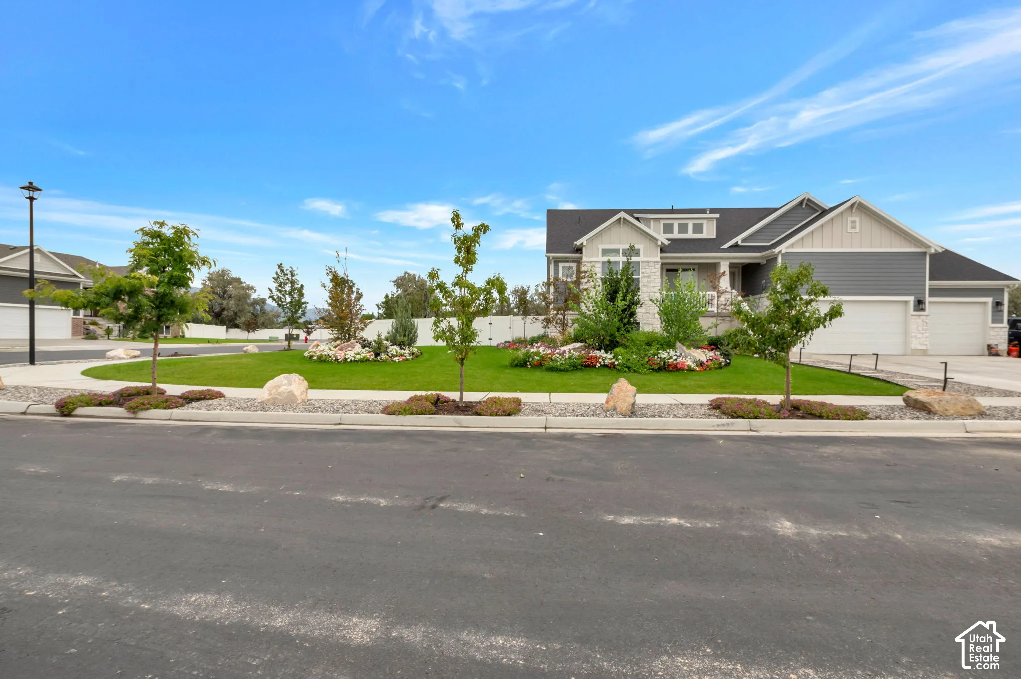 Exterior featuring a stone and siding facade, multiple attached garages, a well-maintained lawn, and established landscaping with mature trees