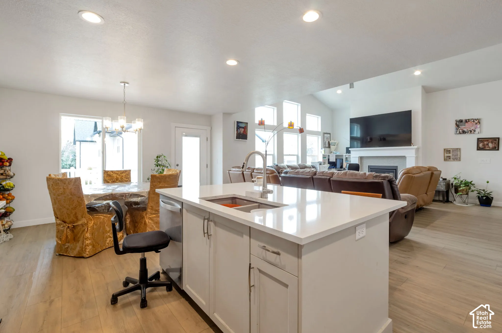 Open-concept living space featuring wood-finish flooring, a kitchen island with a single-basin sink, recessed lighting, vaulted ceilings, and a fireplace with a white mantel