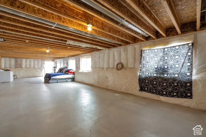 Exposed wood ceiling joists with overhead lighting, concrete flooring, and multiple windows