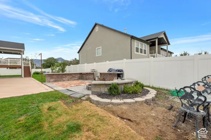 Spacious backyard featuring a built-in fire pit, paved patio, and a covered deck with white railing