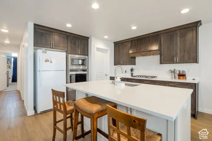 Kitchen featuring dark wood-finish cabinetry, white subway tile backsplash, stainless steel appliances, a center island with white countertops, and recessed lighting