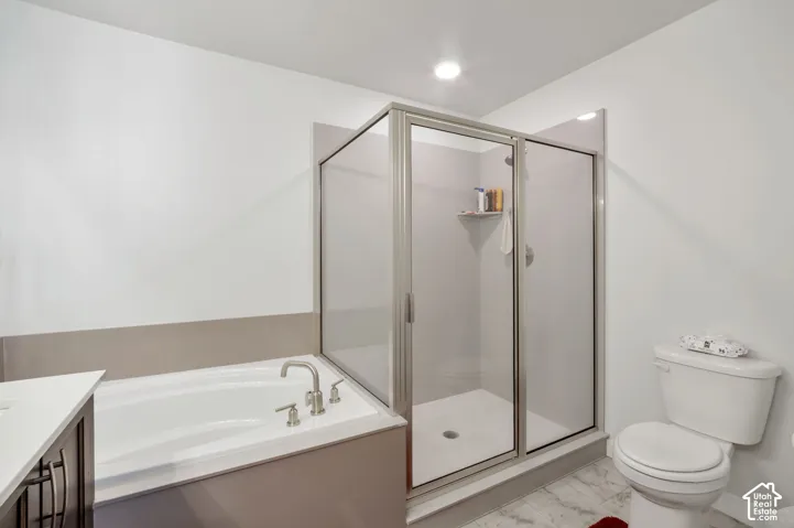 Recessed lighting illuminates the bathroom featuring a built-in tub with brushed nickel fixtures, a glass-enclosed shower, and a white toilet