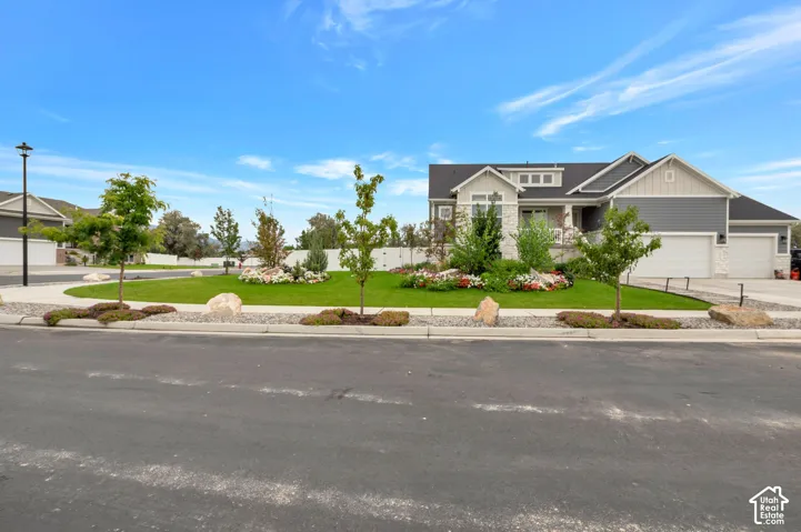 Exterior featuring a stone and siding facade, multiple attached garages, a well-maintained lawn, and established landscaping with mature trees