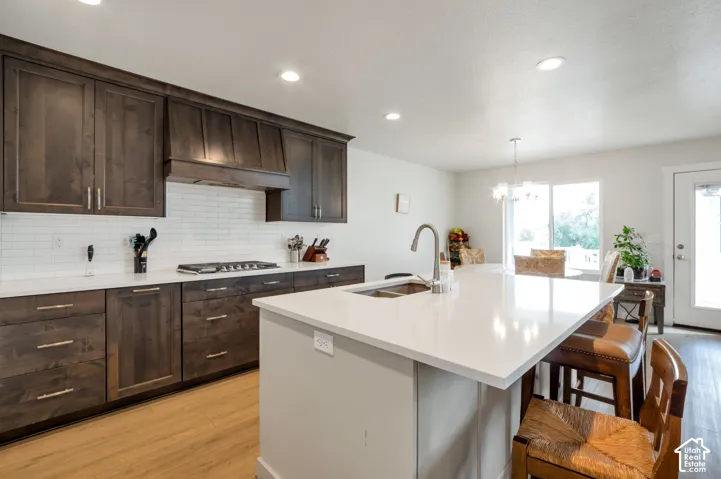 Contemporary kitchen featuring dark wood cabinetry, white subway tile backsplash, a center island with a double basin sink, and wood-finish flooring