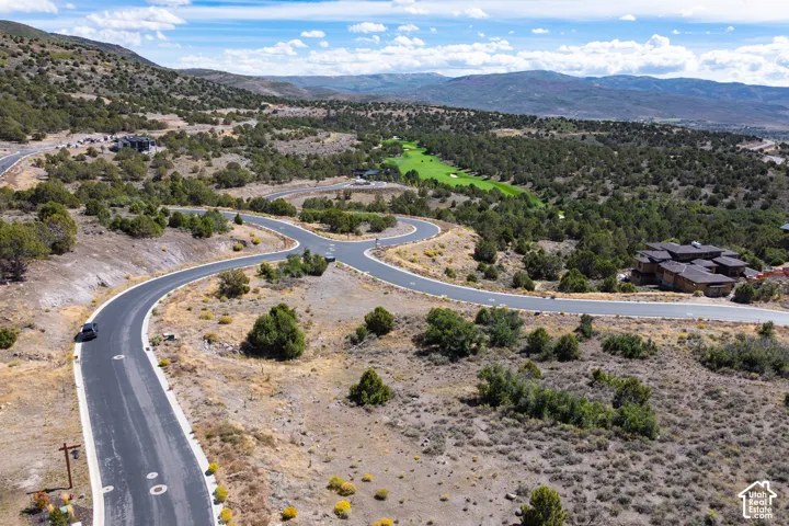 Mountainous terrain with expansive undeveloped land, winding paved roads, distant golf course, and multiple residential structures