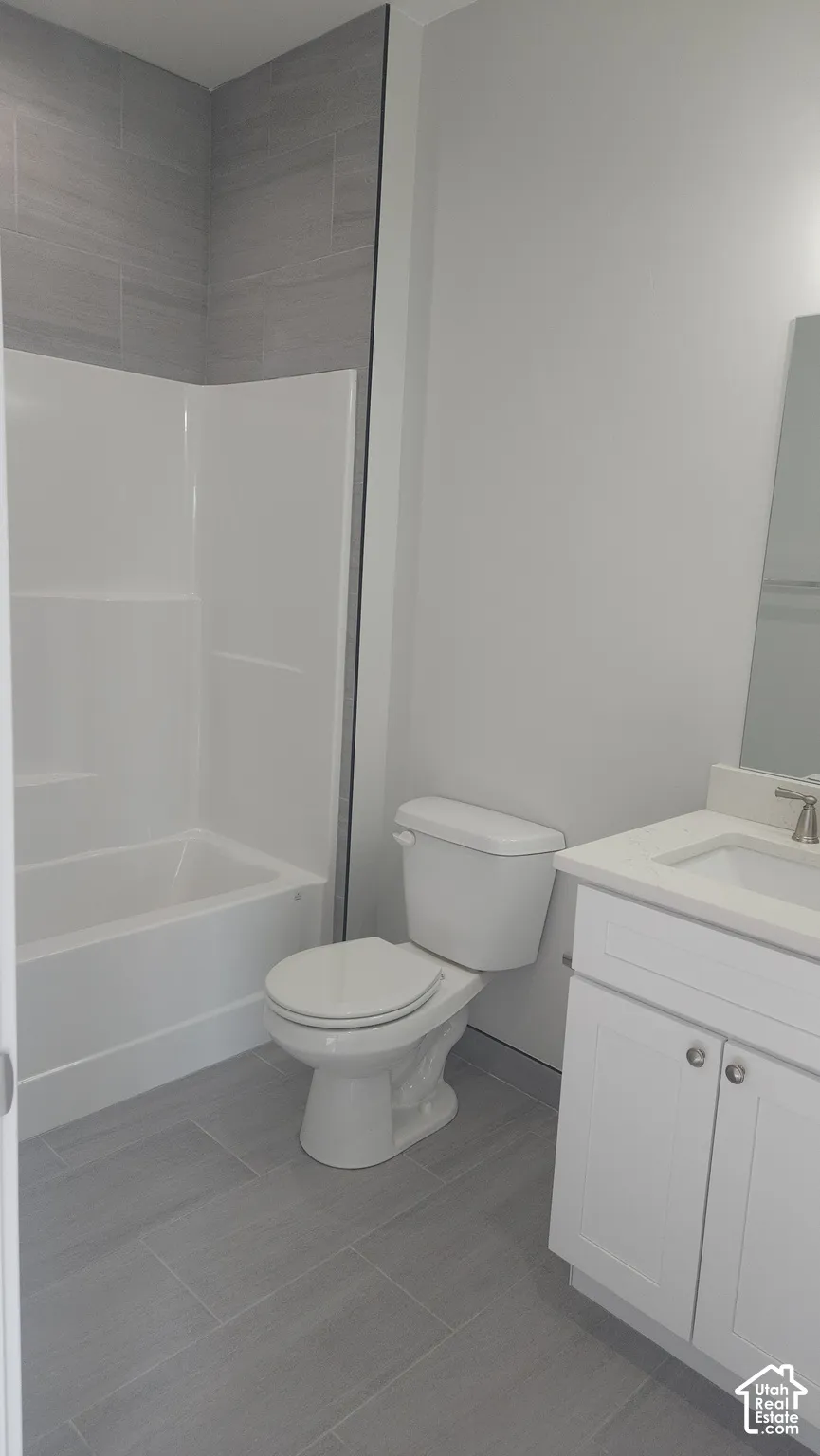 Bathroom with a white bathtub and shower surround, light gray wall tile, white vanity with a light countertop, and light gray floor tiles