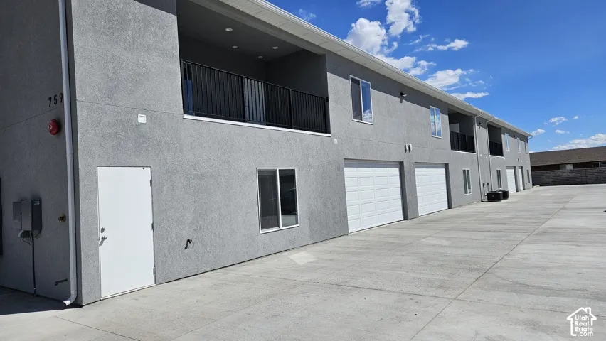 Stucco exterior with multiple garage doors, individual balconies with black railings, and a concrete parking area
