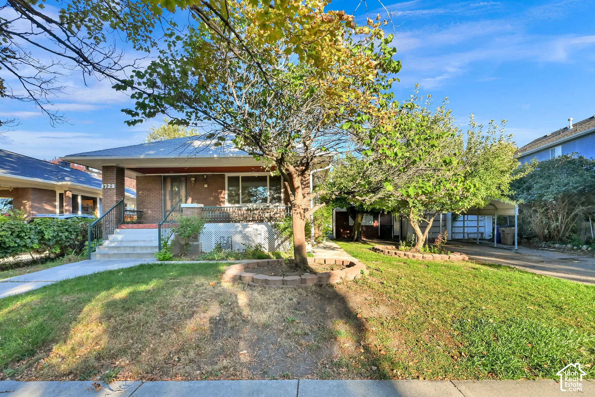 Brick exterior residence featuring a covered front porch, concrete entry stairs with dark railings, and a carport