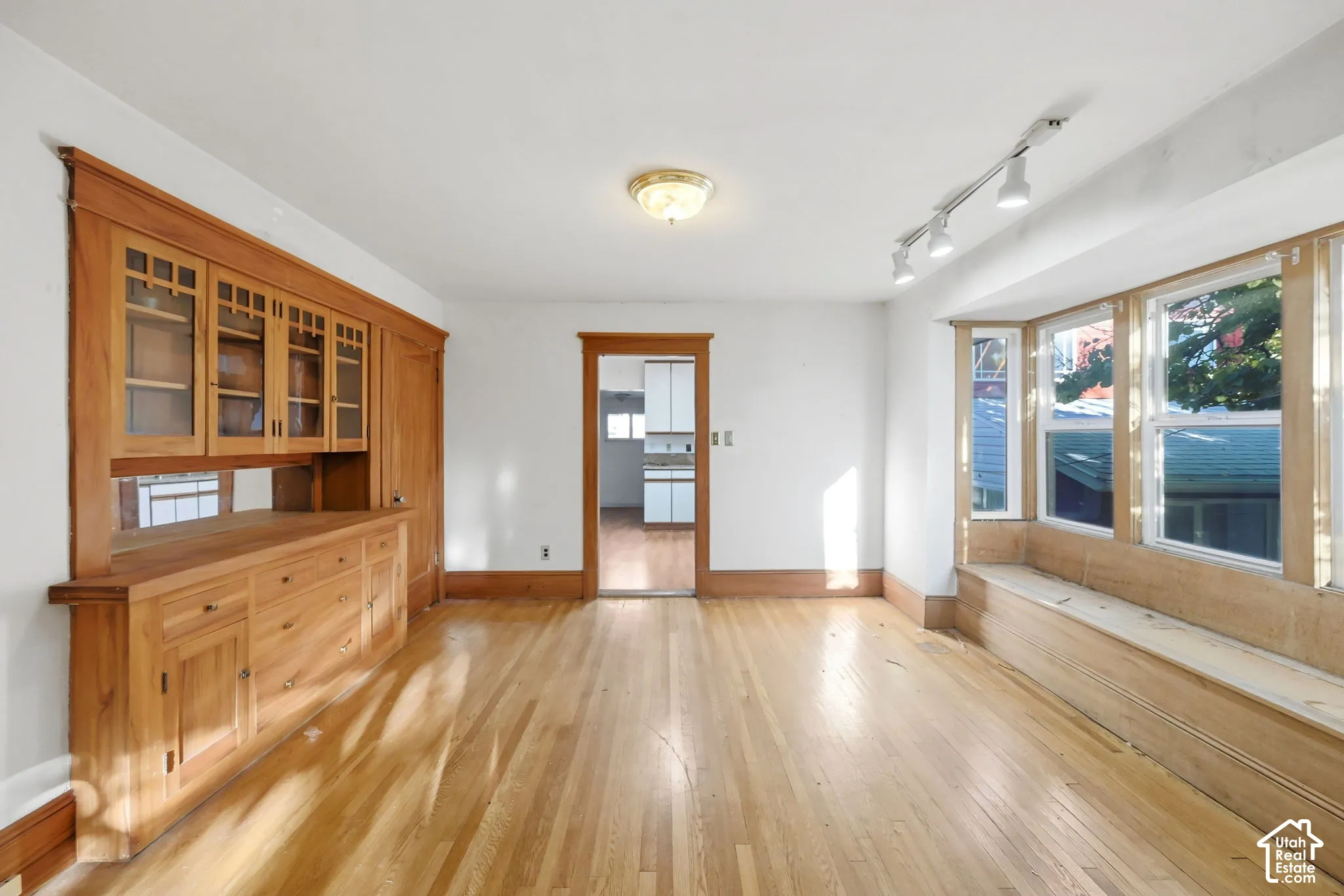 Hardwood flooring, built-in wooden cabinetry with glass-front uppers, track lighting, and a bay window with a built-in bench