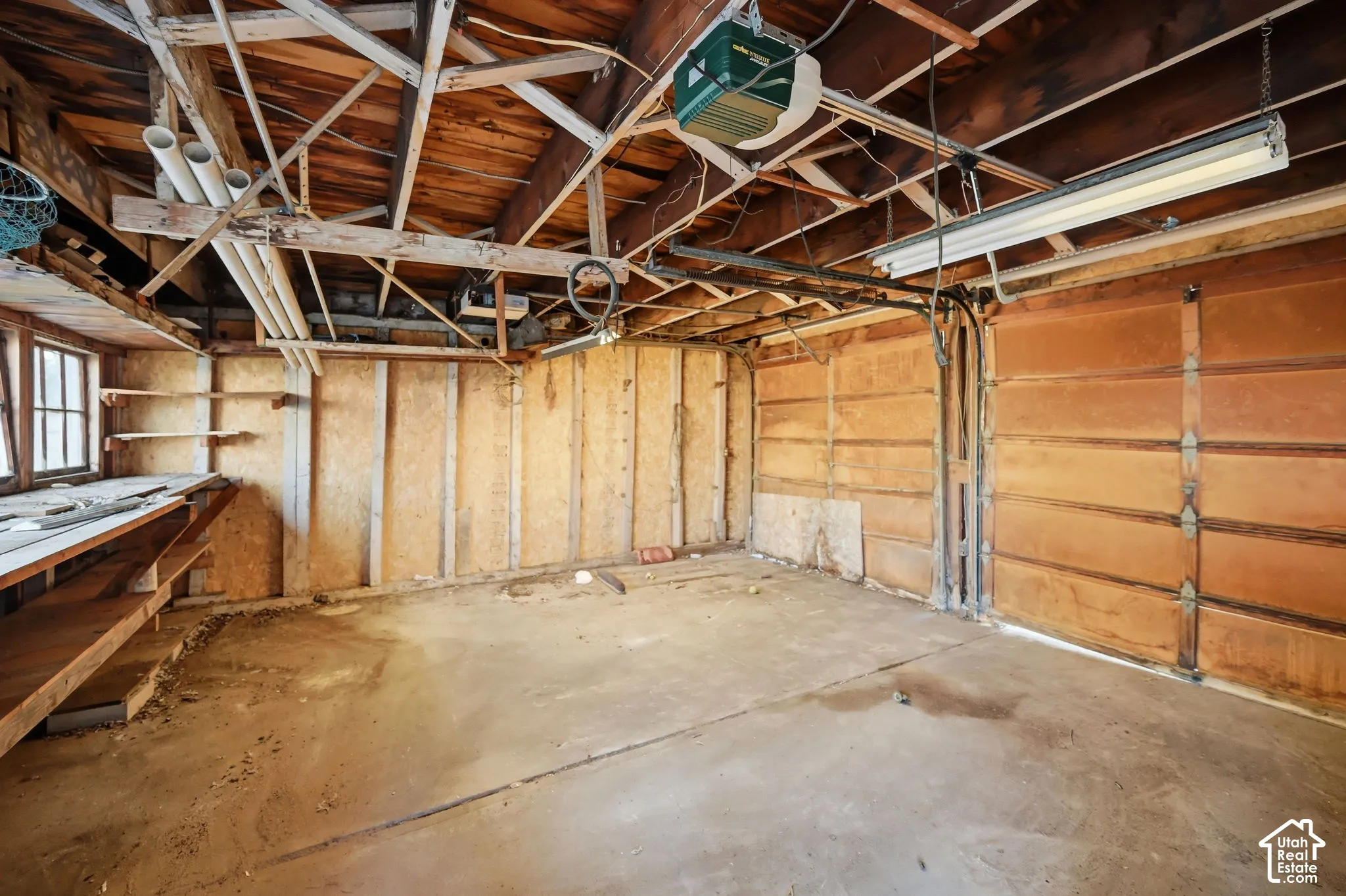 Concrete flooring, exposed wood beam ceiling, built-in shelving, windows, and an overhead garage door with opener