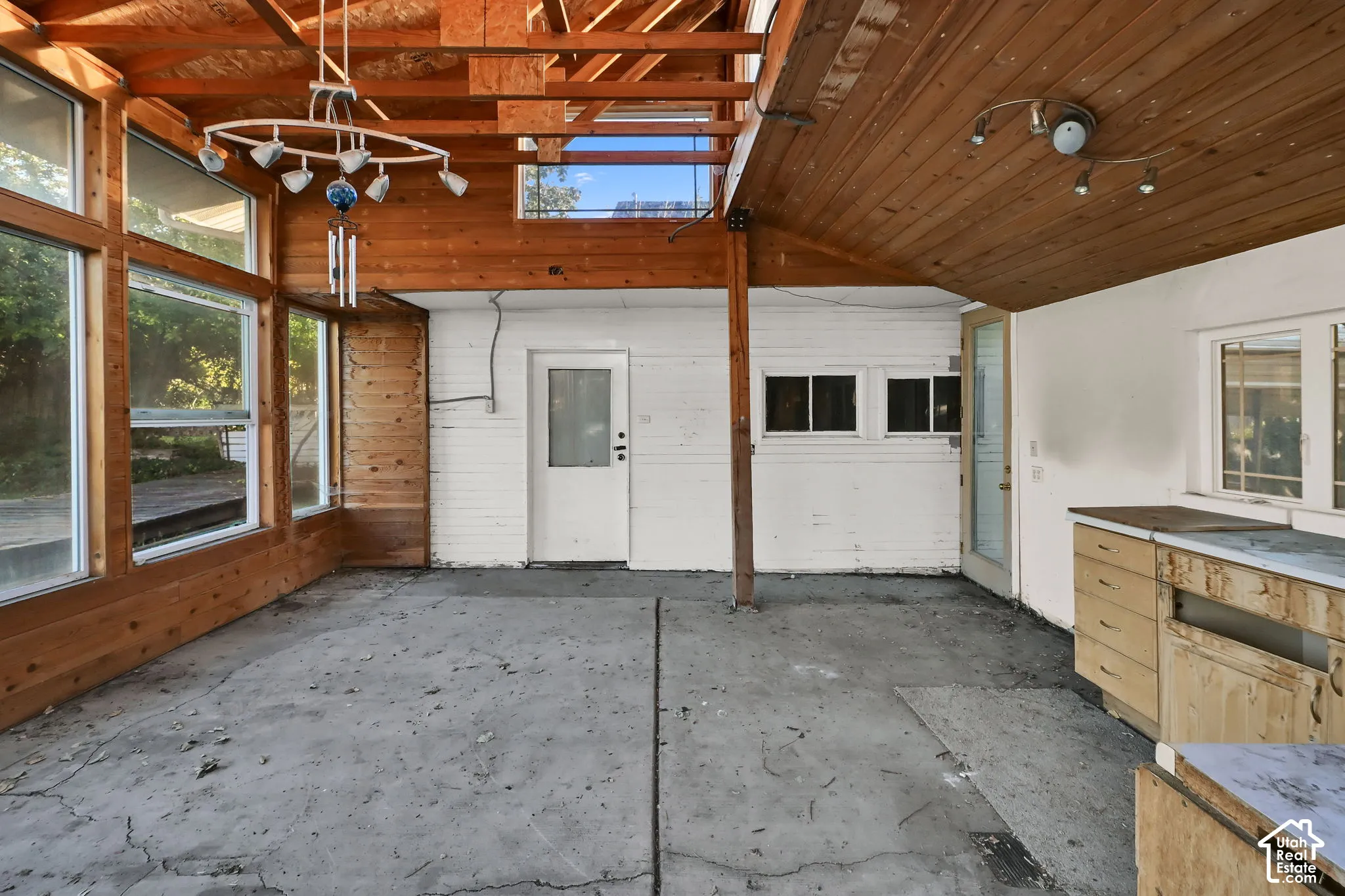 Wood-paneled ceilings with exposed beams, multiple large windows, white painted brick walls, and a concrete floor