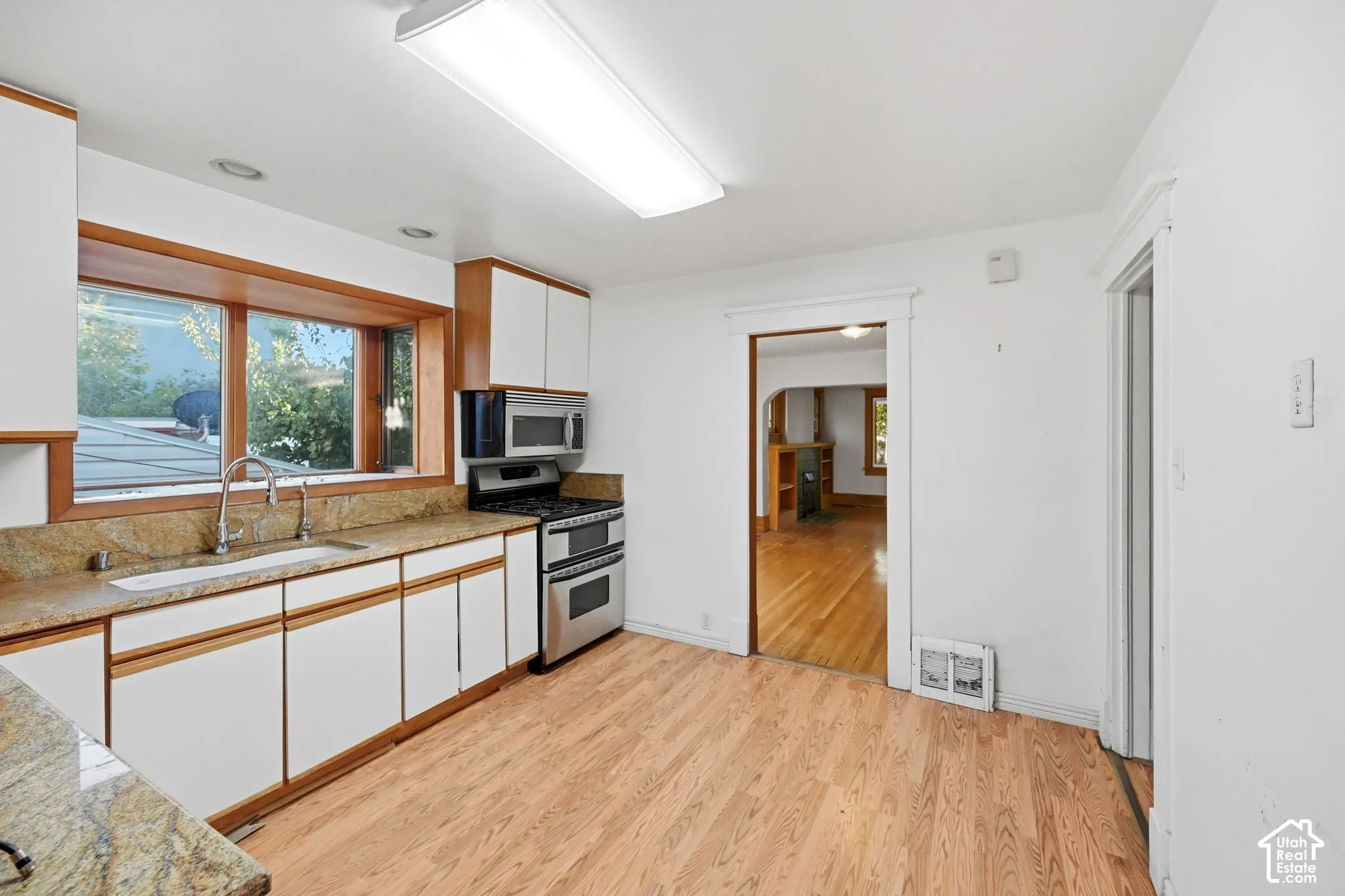 Kitchen featuring light wood-finish flooring, white cabinetry with wood trim, speckled countertops, a stainless steel gas range, and a stainless steel built-in microwave