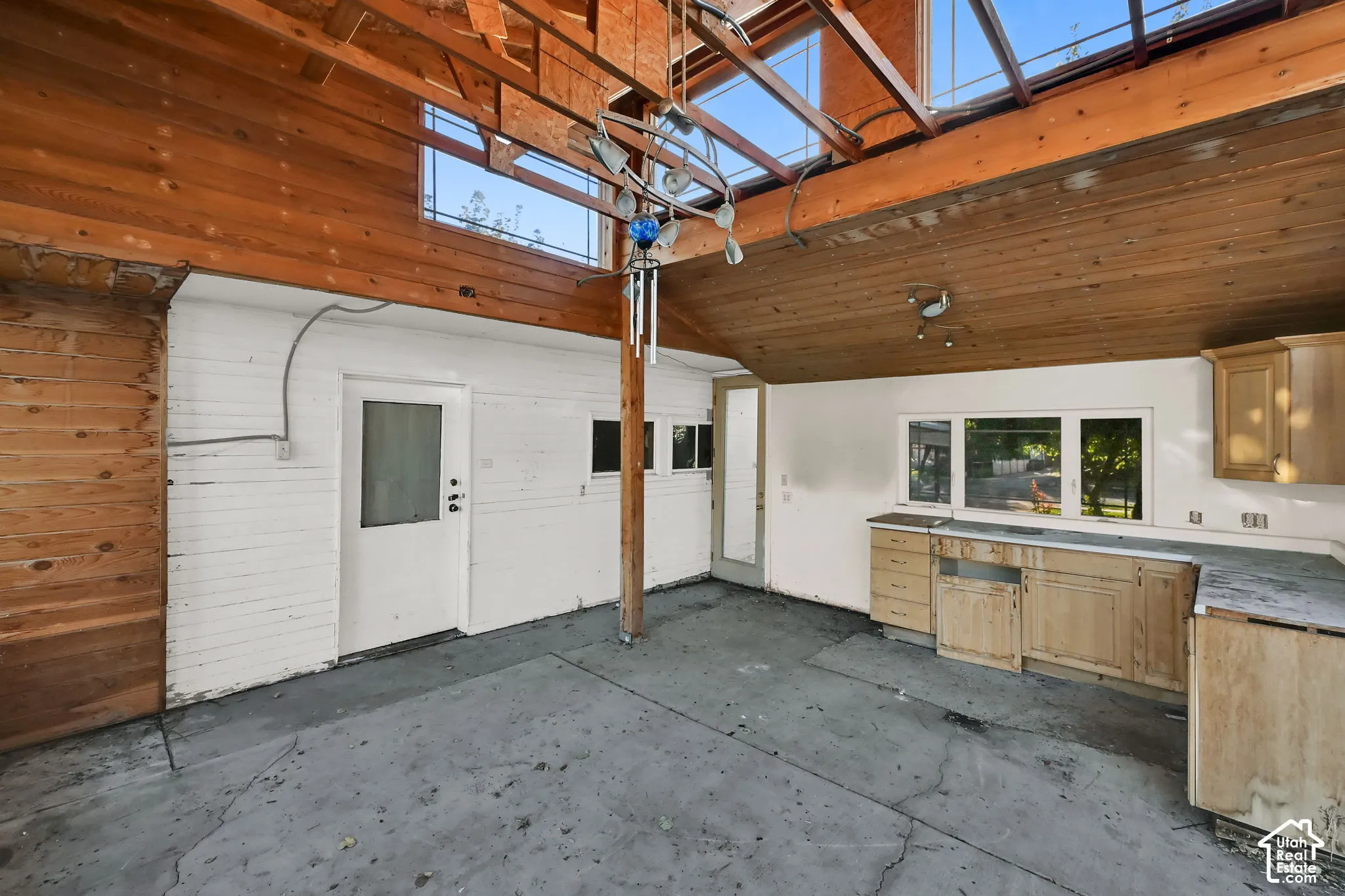 Exposed wood beam ceiling with skylights, white painted brick walls, white entry door, built-in cabinetry, and multiple windows