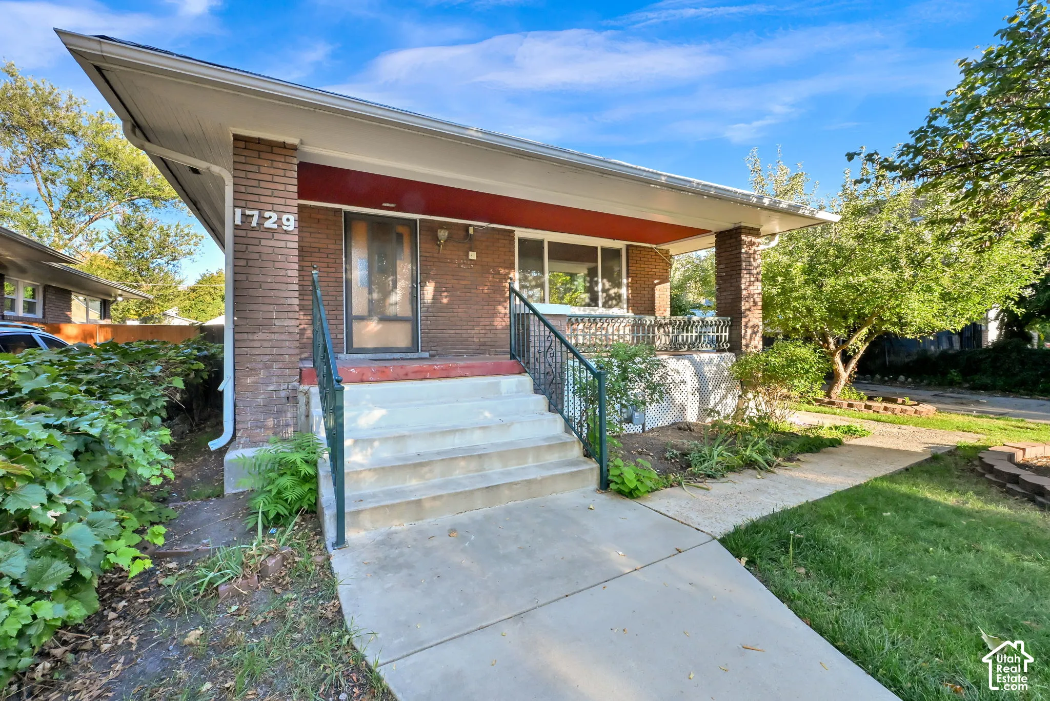 Brick exterior with a covered porch, concrete steps, and a wrought iron railing