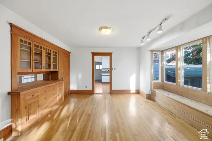 Hardwood flooring, built-in wooden cabinetry with glass-front uppers, track lighting, and a bay window with a built-in bench