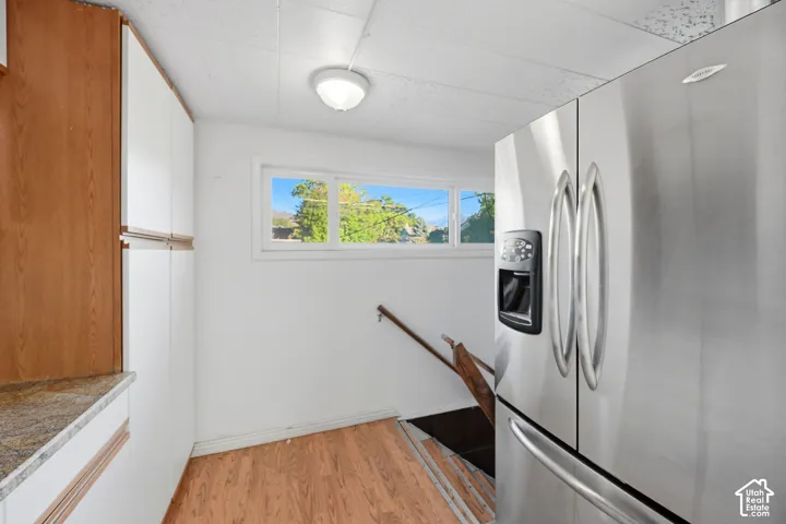 Full-size stainless steel refrigerator, wood-finish flooring, white cabinetry, granite-style countertop, and a double-pane window