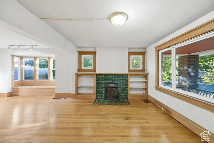 Hardwood flooring, bay window with built-in bench, fireplace with green tile surround, built-in shelving, and wood-trimmed windows