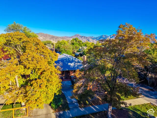 Residential structure with a dark-pitched roof, mountain backdrop, and mature trees with autumn foliage