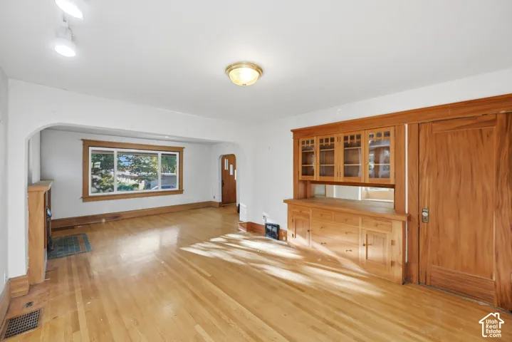 Hardwood flooring, built-in cabinetry with glass panels, wood-frame window, arched doorway, and a decorative fireplace