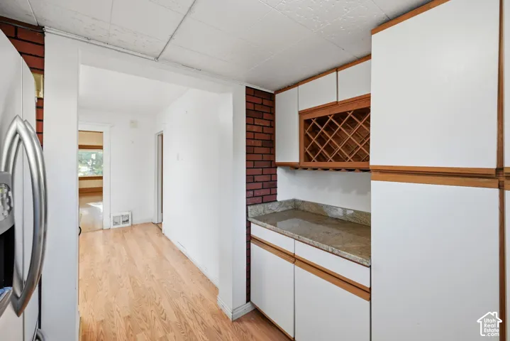 Wood-finish flooring, exposed brick accent wall, white cabinetry with wood trim, built-in wine rack, and granite-style countertop