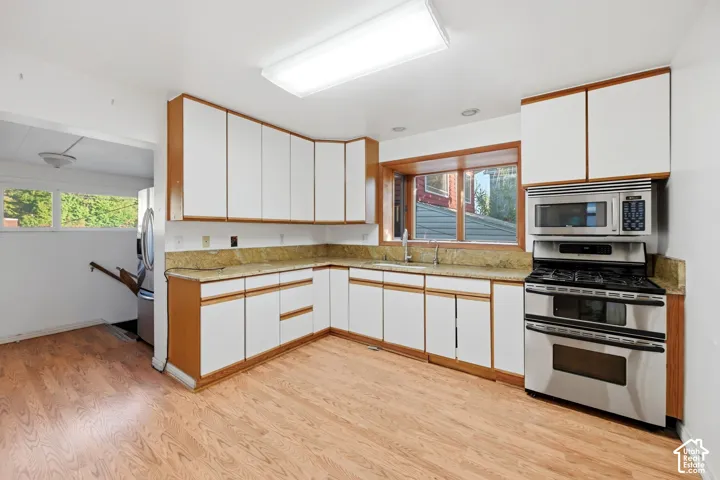 Kitchen featuring wood-finish flooring, white cabinetry with wood trim, stainless steel appliances, and a built-in microwave