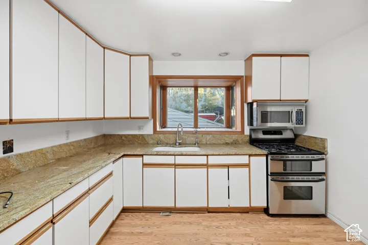Kitchen featuring wood-finish flooring, white cabinetry with wood trim, light-toned countertops, and a stainless steel oven with a microwave