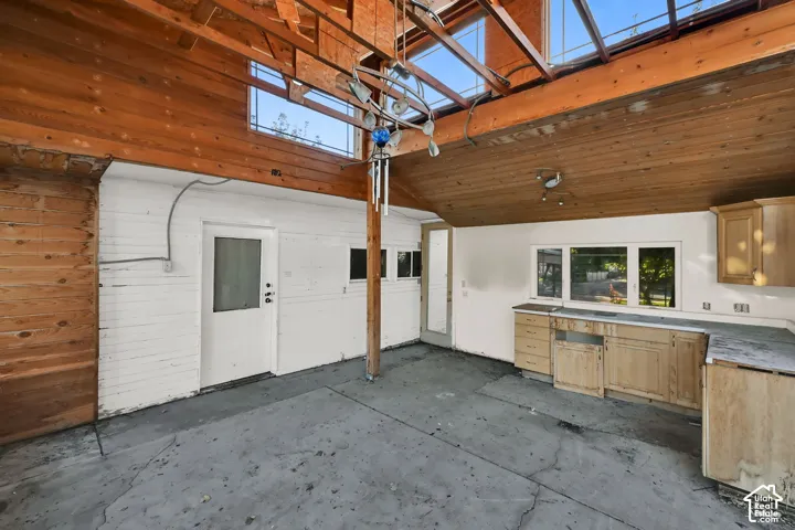 Exposed wood beam ceiling with skylights, white painted brick walls, white entry door, built-in cabinetry, and multiple windows