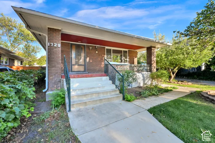Brick exterior with a covered porch, concrete steps, and a wrought iron railing
