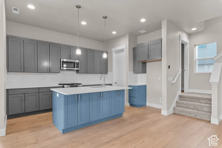Modern kitchen featuring a blue-painted center island with pendant lighting, stainless steel appliances, grey cabinetry, and white subway tile backsplash