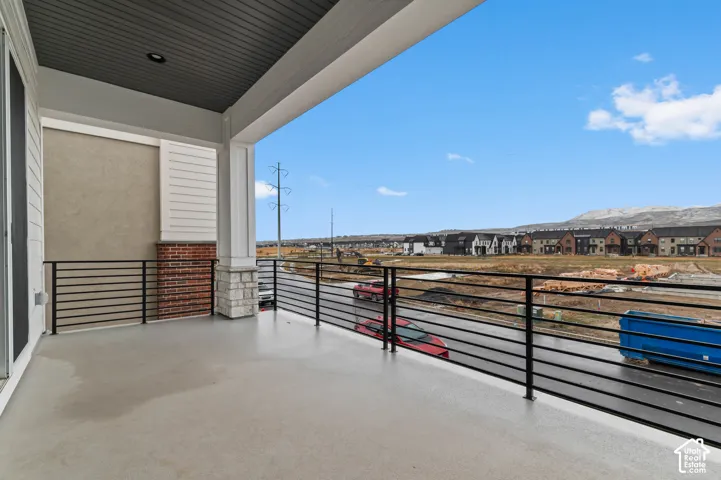 Spacious covered balcony featuring a concrete surface, black horizontal railings, and a stucco and brick exterior wall