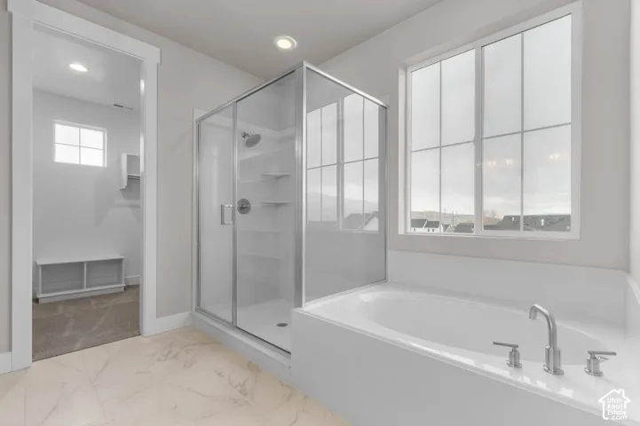 Integrated soaking tub with brushed nickel fixtures, glass-enclosed shower, large multi-pane window, recessed lighting, and light-toned tile flooring