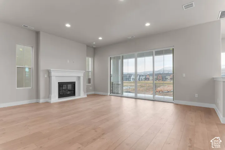 Wood-finish flooring, white fireplace mantel, gas fireplace insert, recessed lighting, and large sliding glass doors