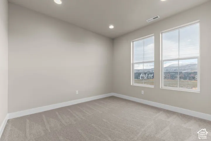 Neutral wall paint with recessed ceiling lighting, two large windows, and light-colored carpet flooring