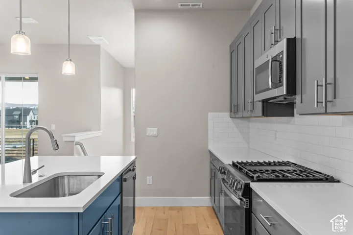 Kitchen featuring a stainless steel sink with a gooseneck faucet, white countertops, blue base cabinetry, grey wall cabinets, and stainless steel appliances