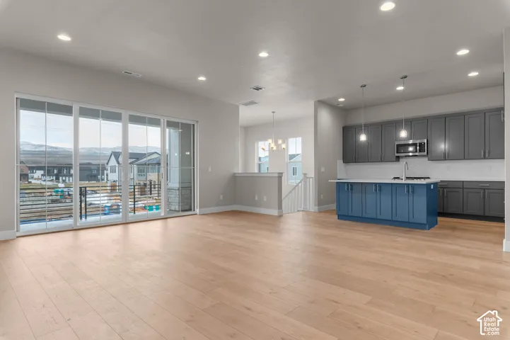 Open-concept living area featuring light wood-finish flooring, a full wall of sliding glass doors, recessed lighting, and a kitchen with gray cabinetry, a blue island, and stainless steel appliances