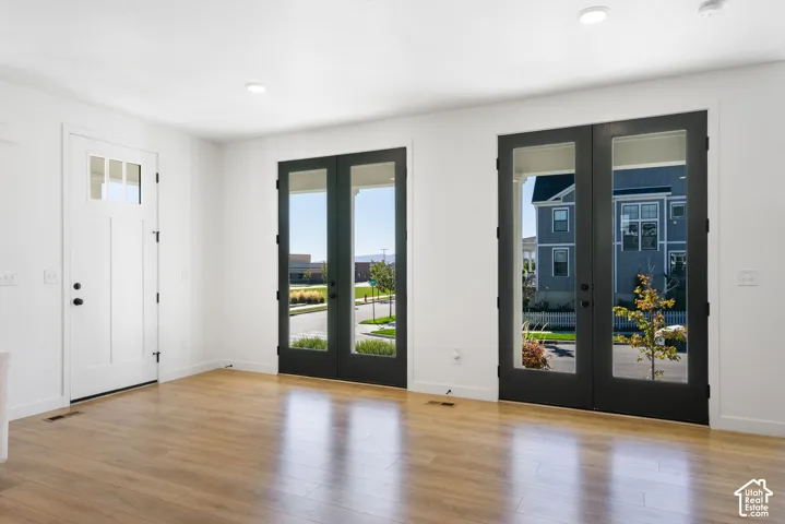 White entry door with black hardware, wood-finish flooring, recessed lighting, and two sets of black-framed glass-paneled doors