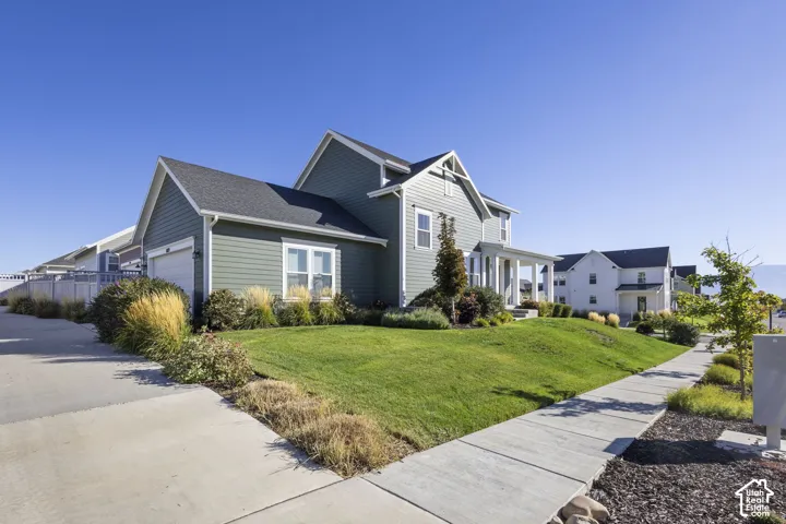 Green siding exterior with a prominent front porch, attached garage, and a manicured lawn